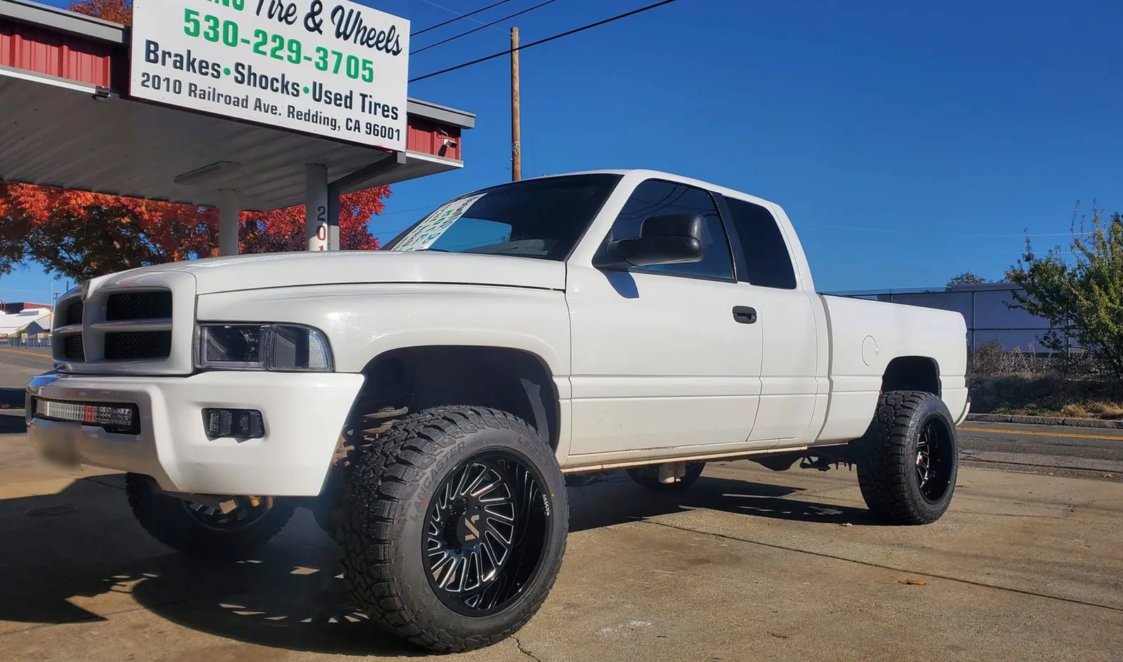Lifted white Ram pickup on black machined wheels and all-terrain tires outside Redding Tires and Wheels