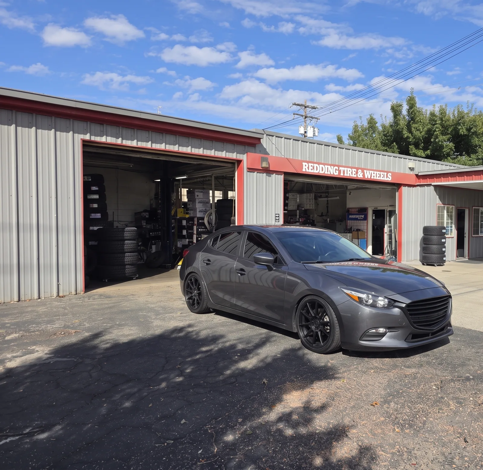Lowered gray sedan on black wheels outside the Redding Tires and Wheels bays