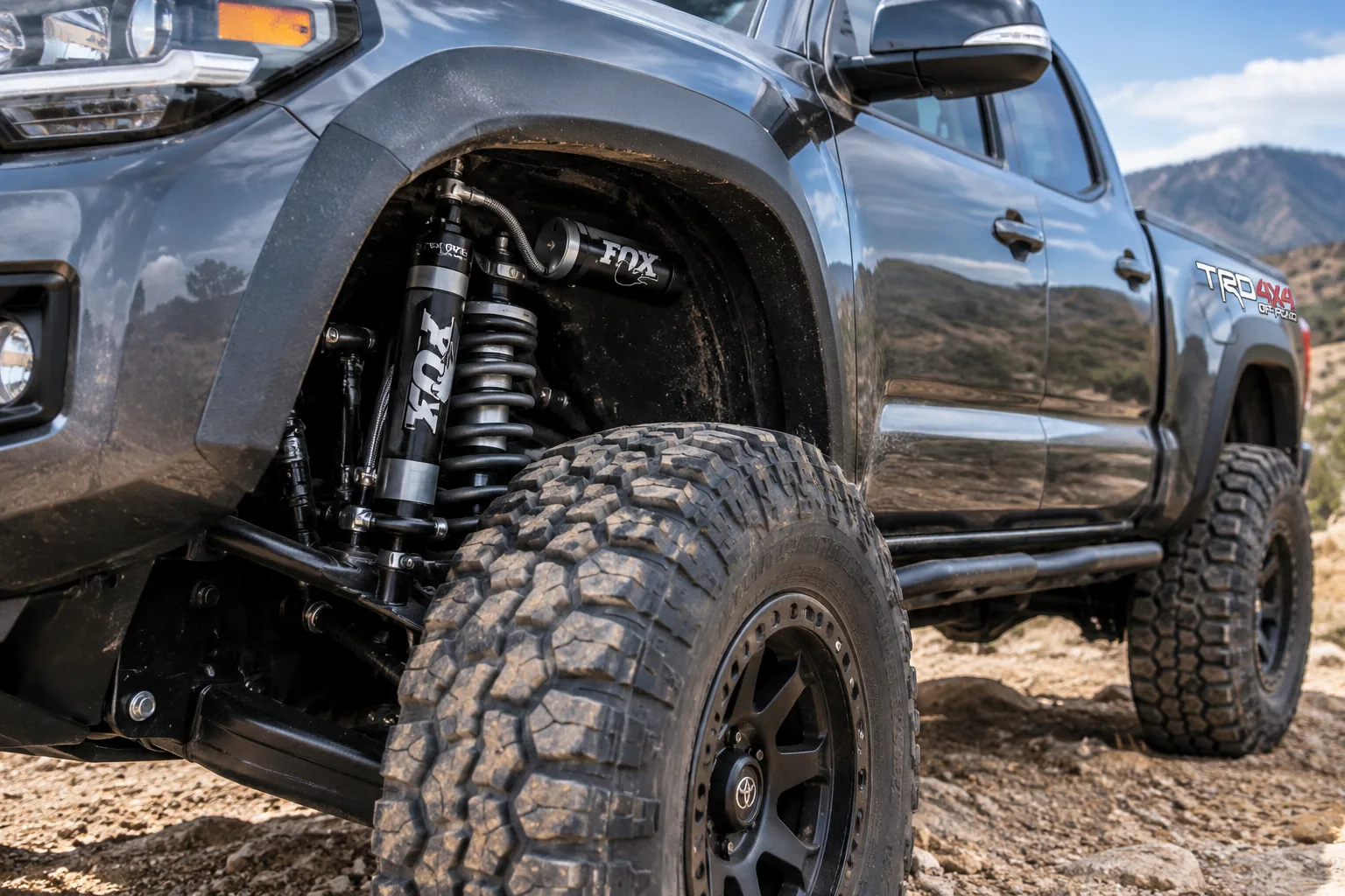 Lifted gray pickup with an off-road coilover shock and remote reservoir behind a mud-terrain tire